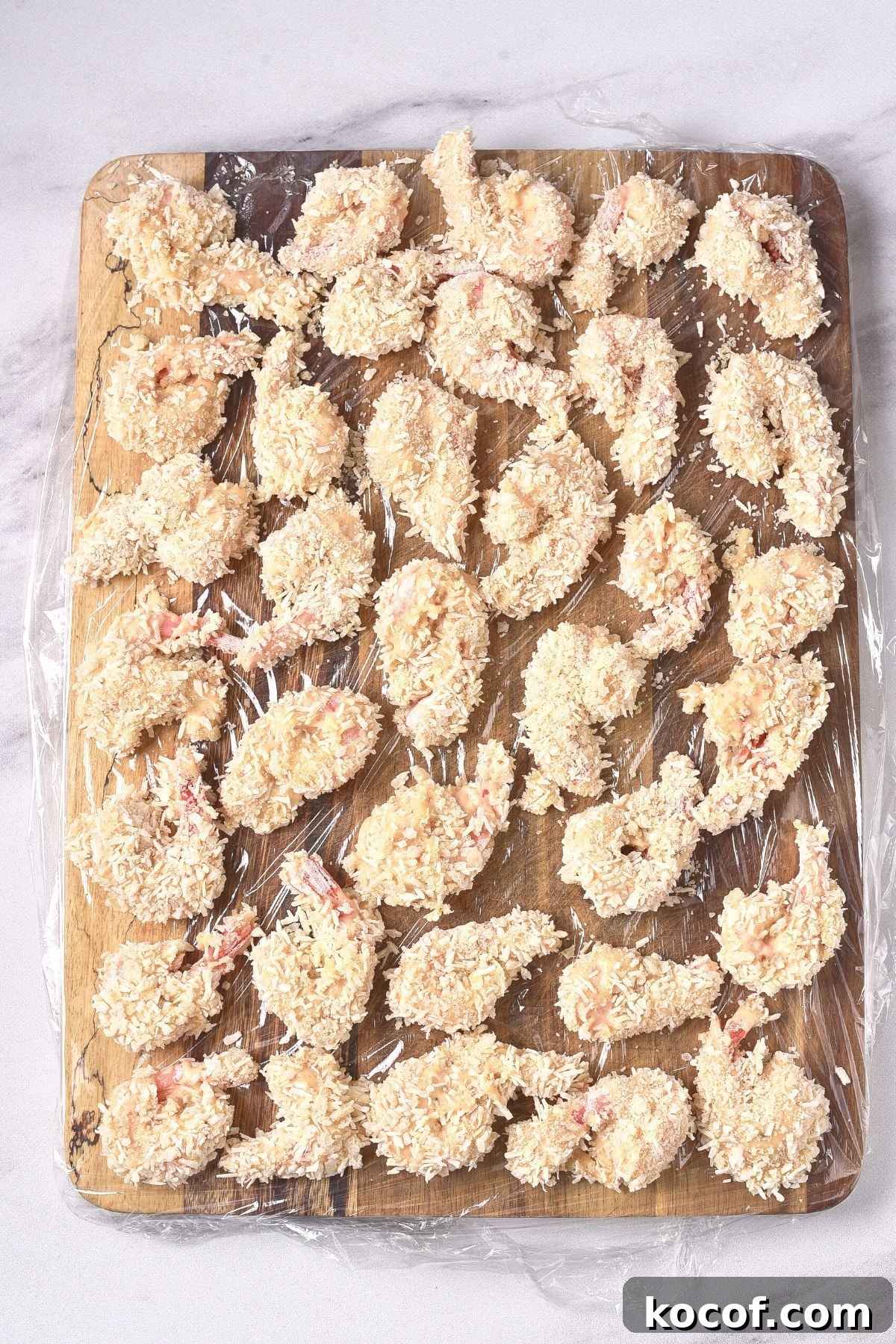 GF Coconut Shrimp (dairy-free) Freshly breaded shrimp on plastic-lined wooden board.