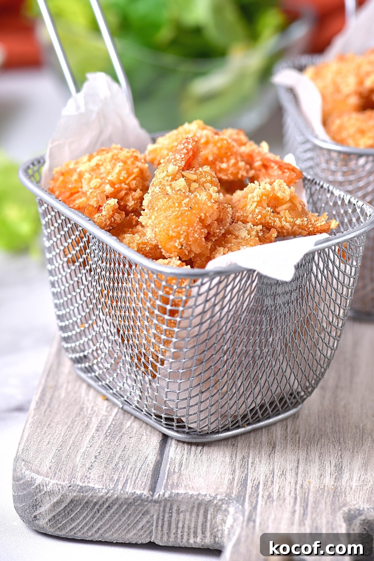 GF Coconut Shrimp (dairy-free) A basket of crispy gluten-free fried shrimp on wooden board.