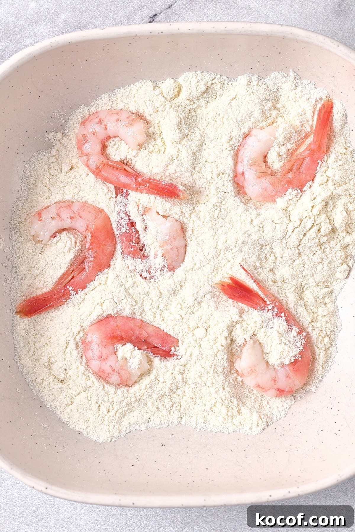 Coconut Fried Shrimp Recipe Coating fresh shrimp in flour in a bowl.