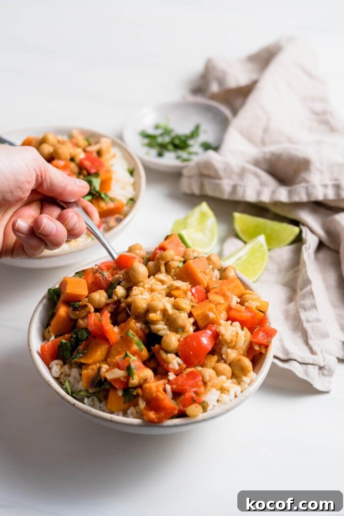 Hand using a spoon to take a spoonful of sweet potato curry from a bowl.