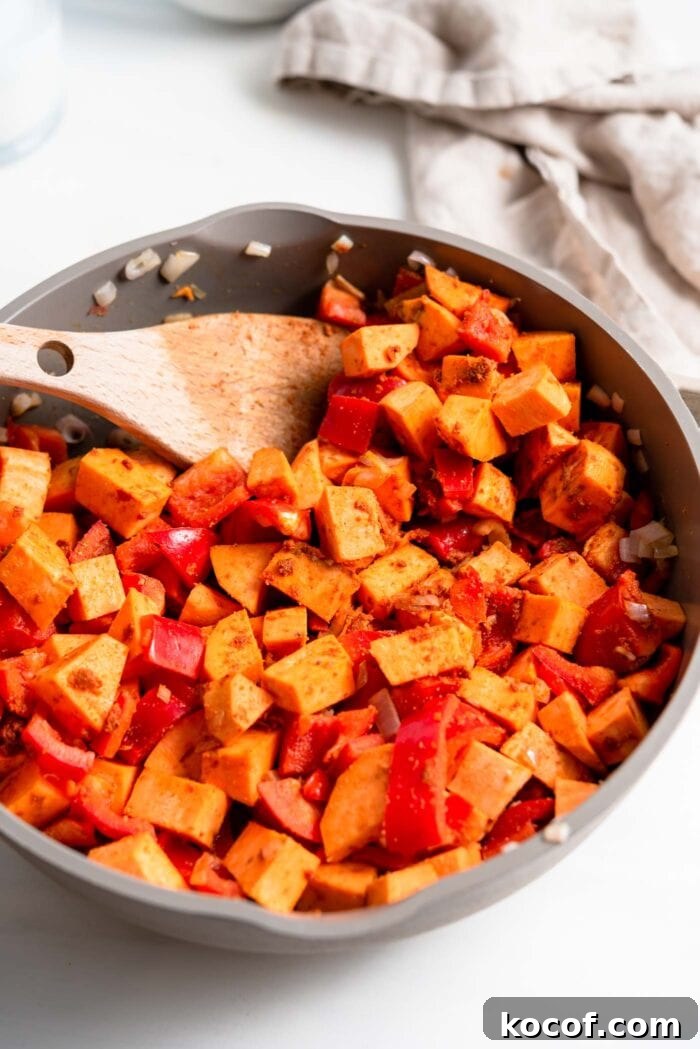 Sweet potato and bell pepper cooking in spices in a skillet.