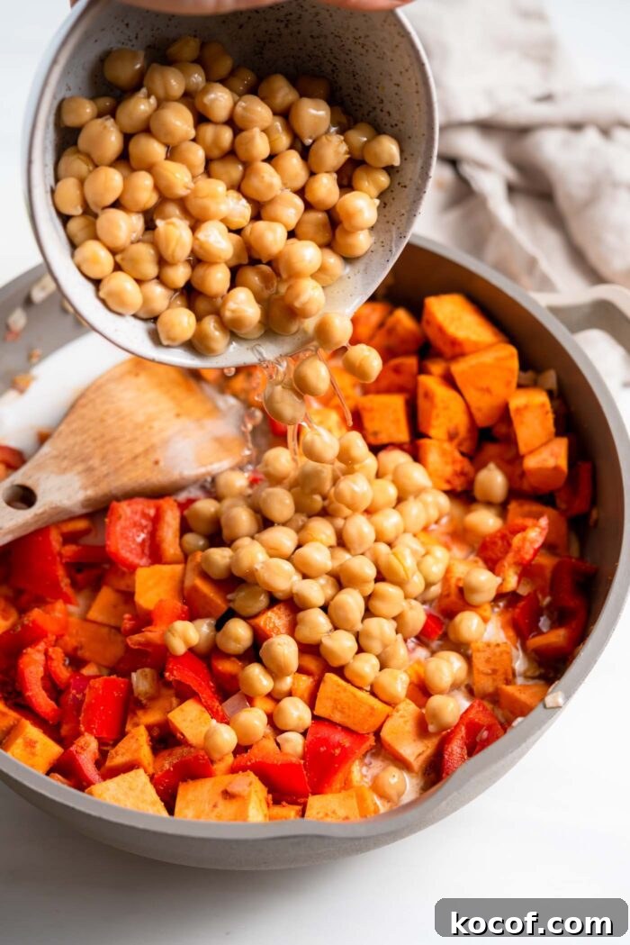 Dumping a bowl of chickpeas into a skillet of sweet potato and bell pepper.