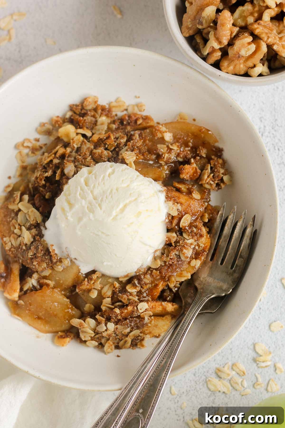 Apple crisp topped with a scoop of ice cream in a small bowl with a small bowl of walnuts on the side.