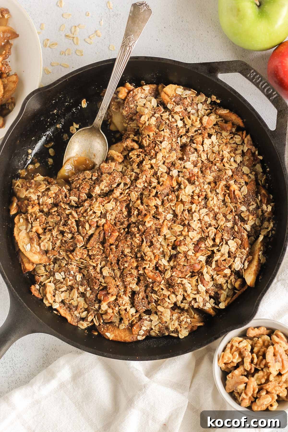 Apple crisp in a cast iron skillet with some taken from the side of the skillet and a serving spoon in the skillet scooping up some of the apples.