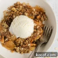 Single serving of apple crisp in a small bowl topped with a scoop of vanilla ice cream with 2 vintage forks in the bowl.