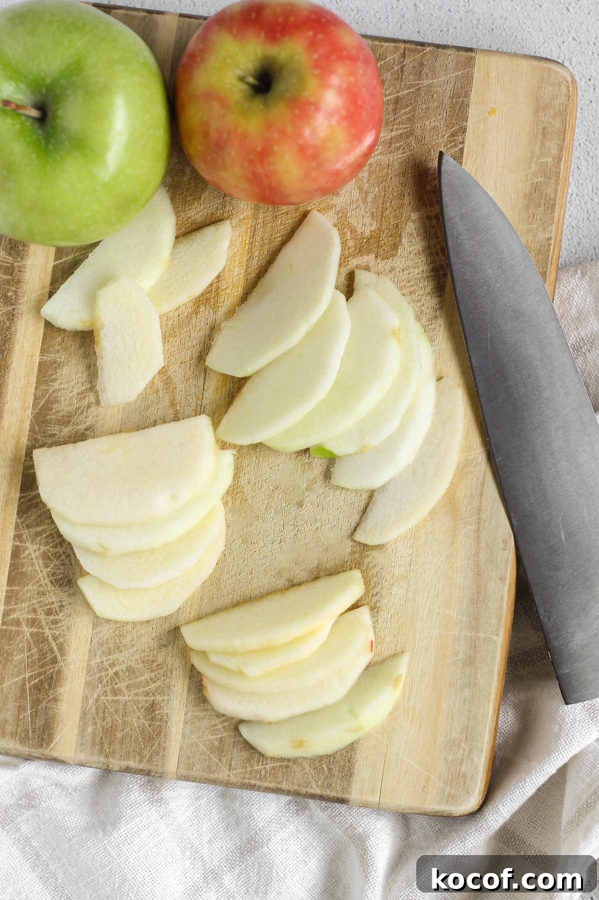 Apple slices and whole apples on a wood cutting board with a large chopping knife.