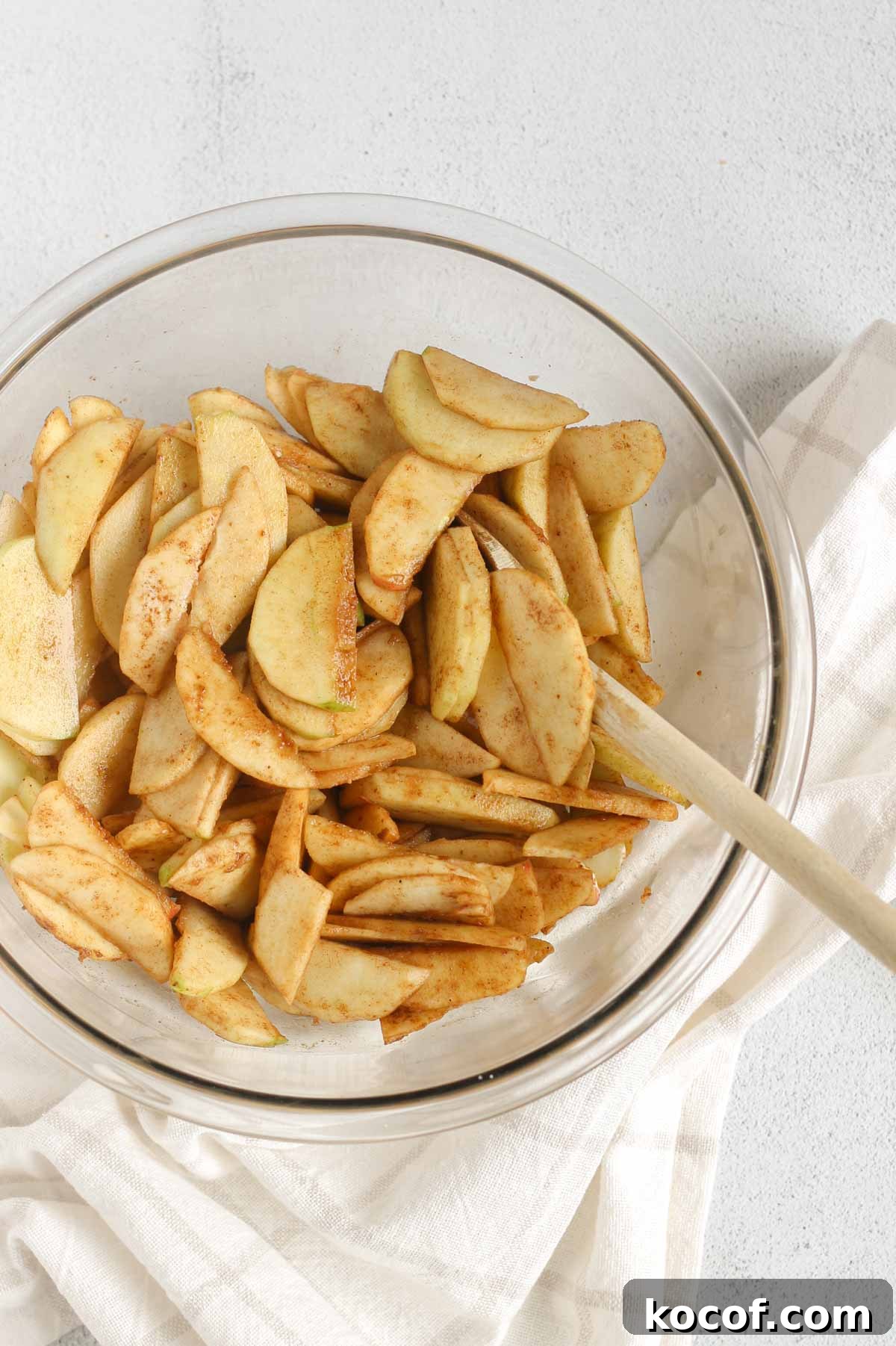 Sliced apples mixed with cinnamon and sugar in a large glass mixing bowl.