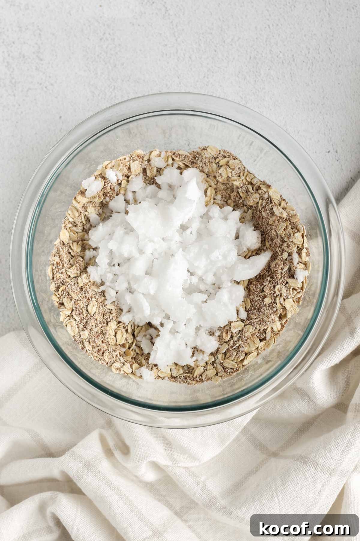 Apple crisp topping mix with pieces of coconut oil on the top in a glass mixing bowl.