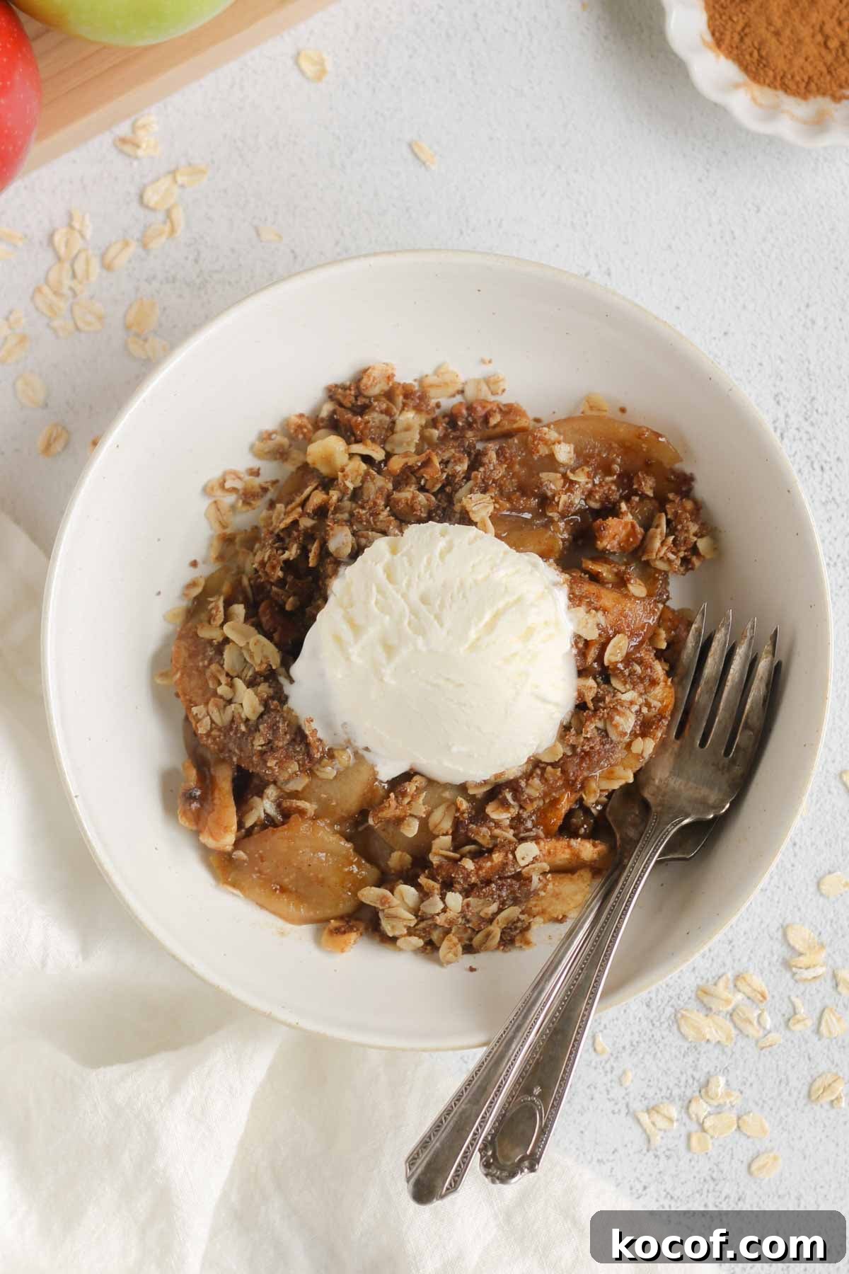 Apple crisp topped with a scoop of ice cream in a small bowl with two vintage forks in the bowl.