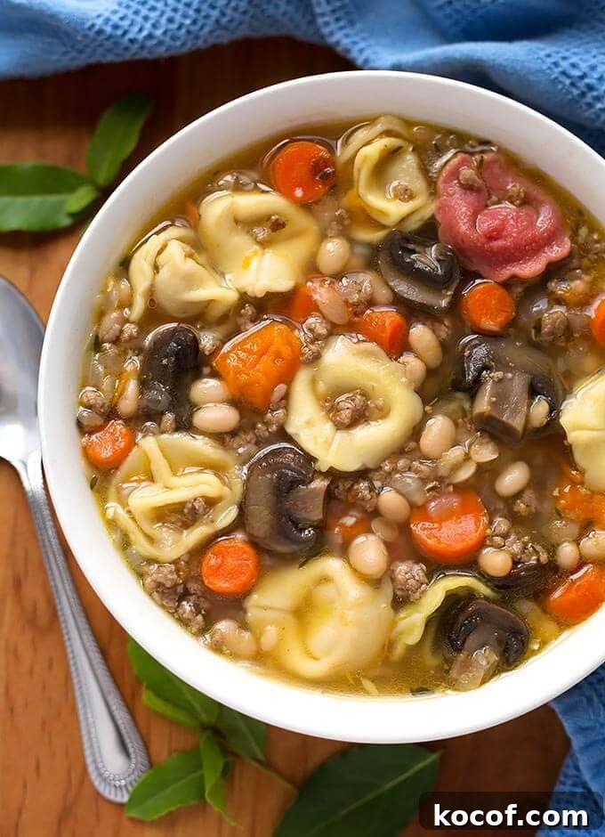Tortellini Soup in a white bowl on wooden board with spoon