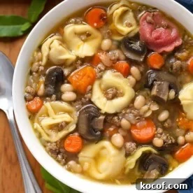 Tortellini Soup in a white bowl on wooden board with spoon