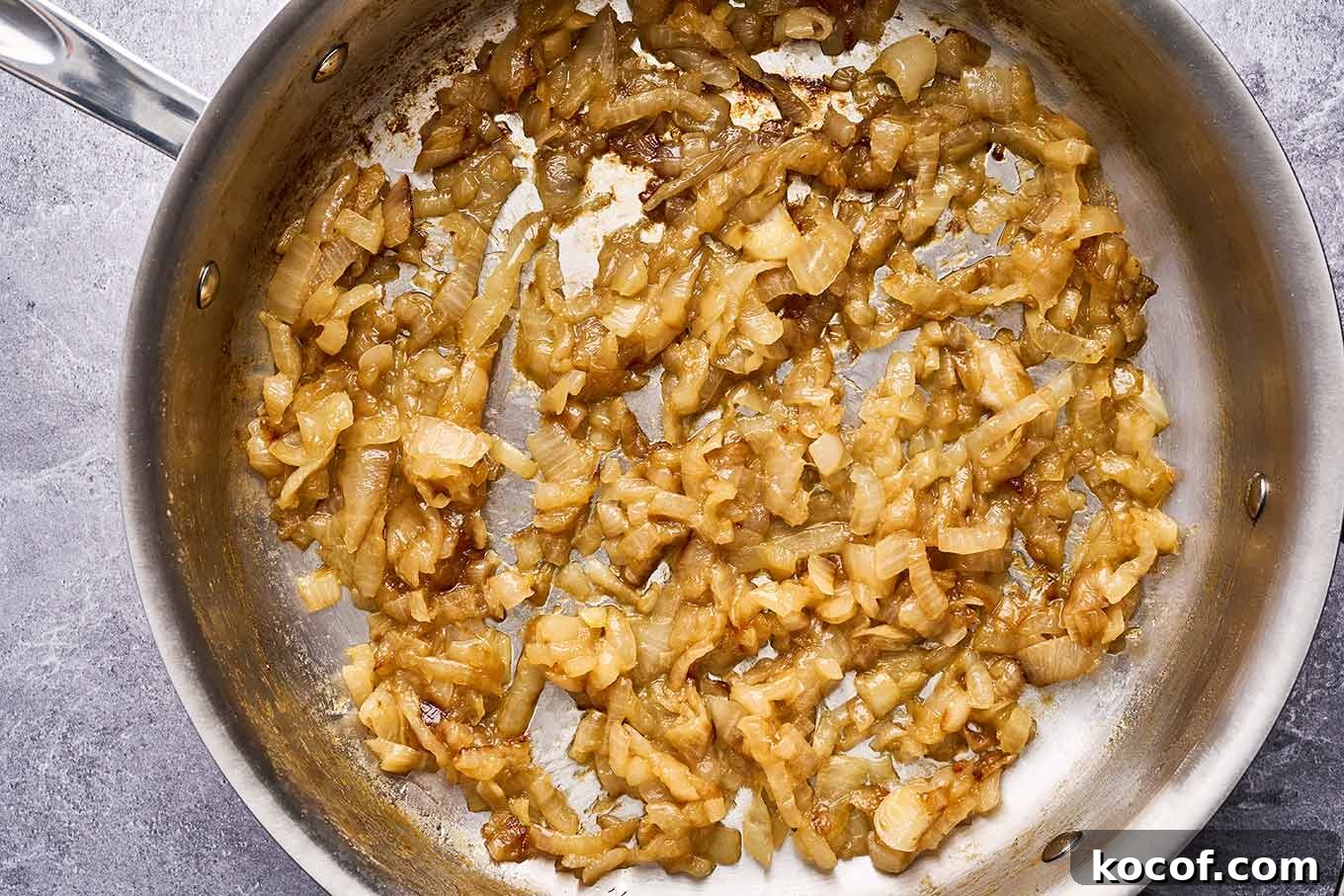 Caramelized onions cooking in a stainless pan for pasta with caramelized onions and sausage.