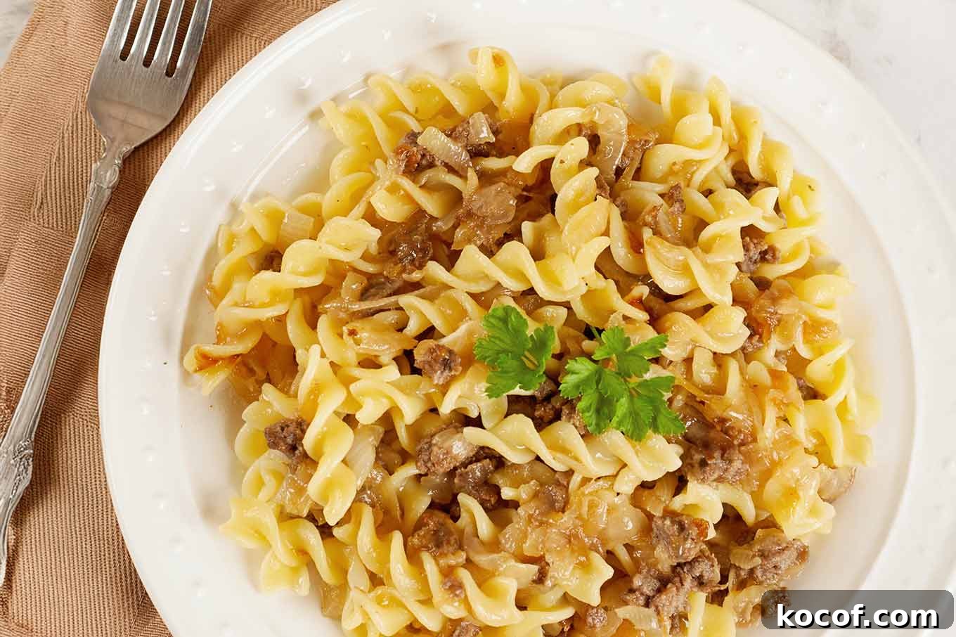 A plate of rotini pasta with caramelized onions and Italian sausage, topped with parsley.