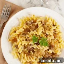 Pasta with caramelized onions and Italian sausage served on a white plate, garnished with parsley.