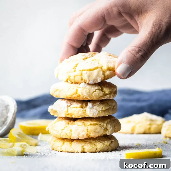 Hand stacking up 5 lemon crinkle cookies with lemon slices garnished around them.