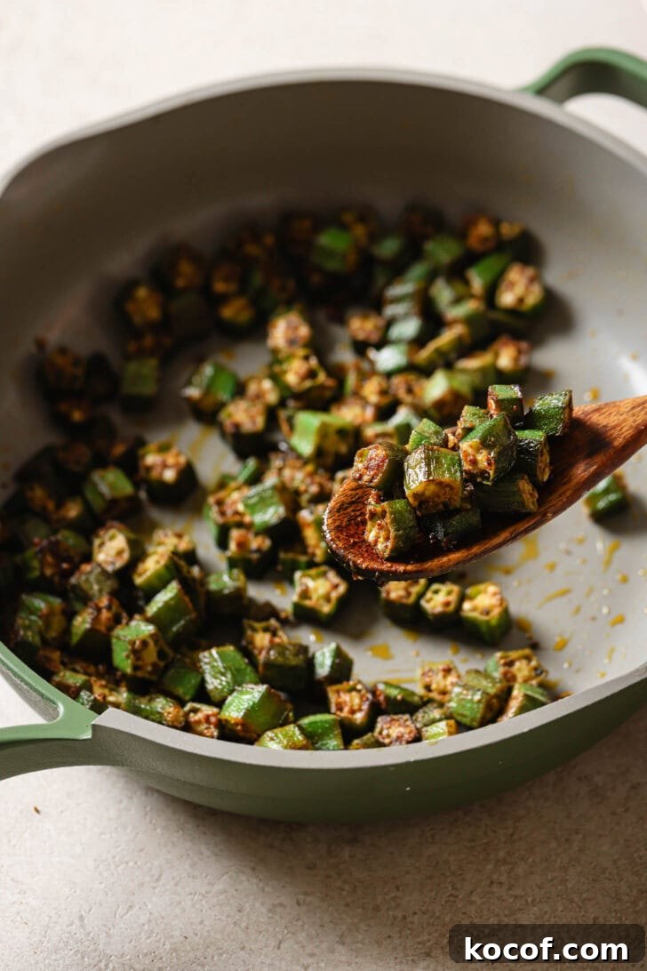 Holding a spoonful of Bhindi Fry over a skillet.