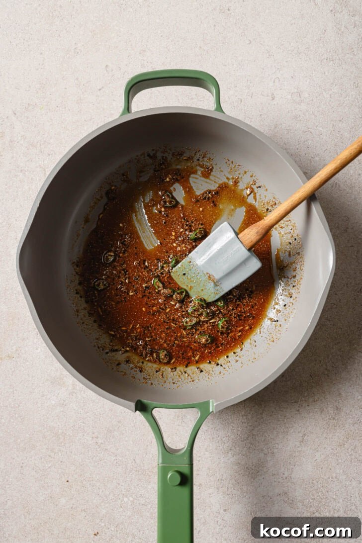 Green chilies added to sauteéd spices in skillet to make Bhindi Fry.