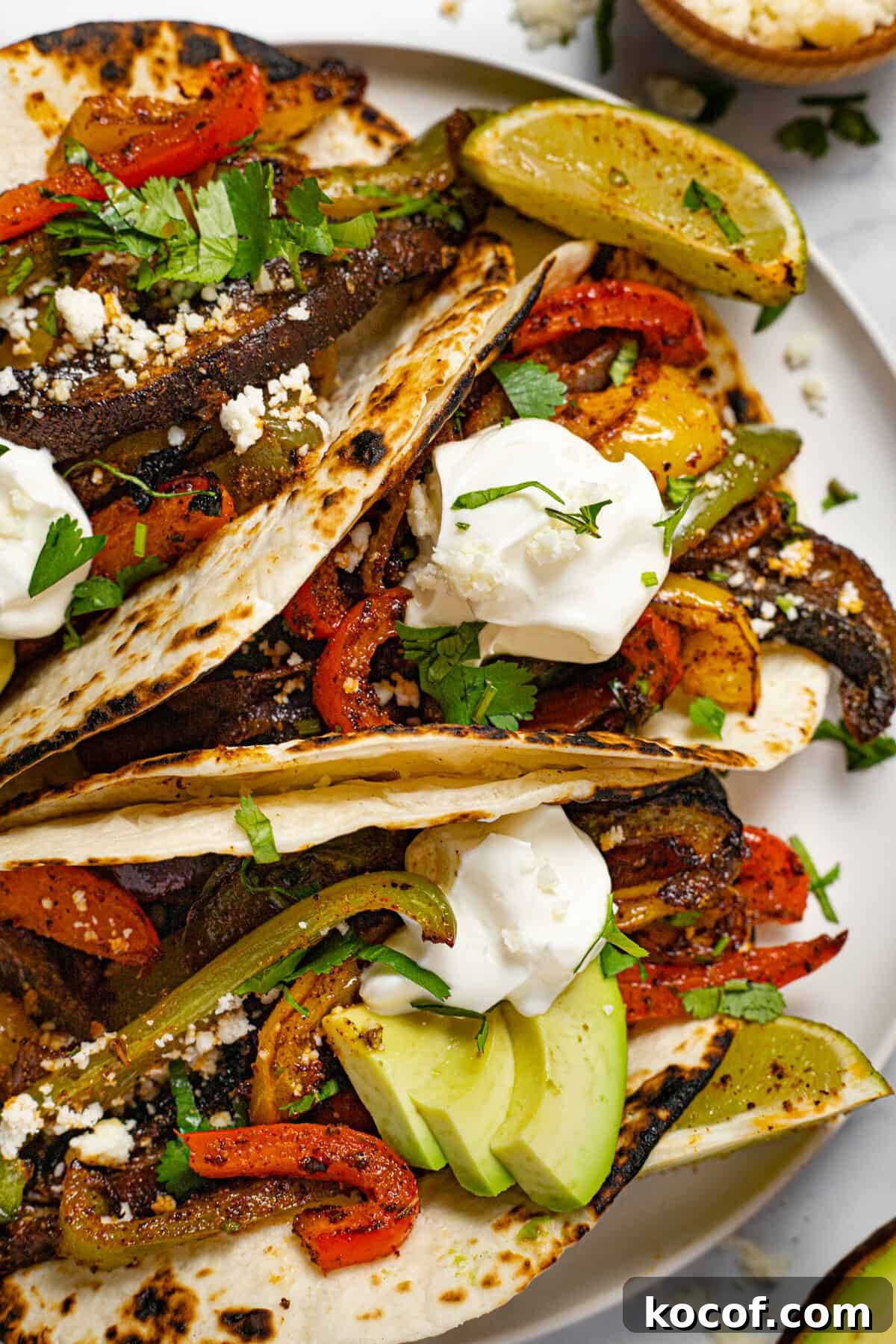 White plate with three fajitas topped with sour cream and fresh cilantro