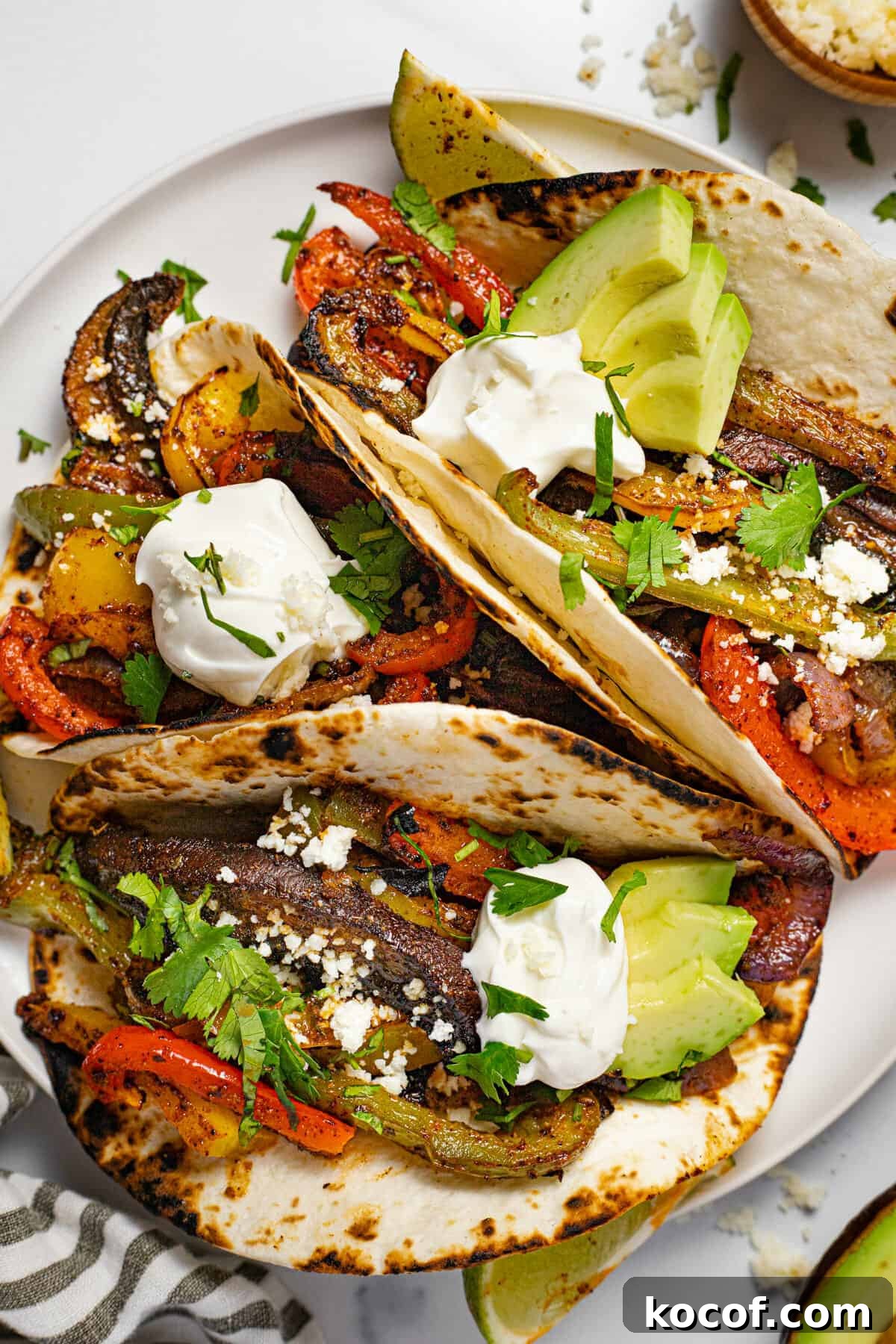White plate with three fajitas topped with sour cream and fresh cilantro