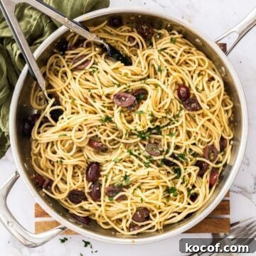 Large frying pan with Anchovy and Olive Pasta sitting on a wooden board, with some tongs in the pan.