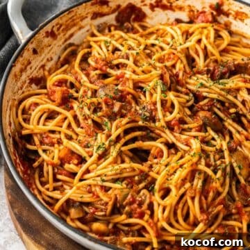 Mushroom and Tomato Pasta, garnished with finely chopped parsley, in a large skillet, sitting on a wooden board.