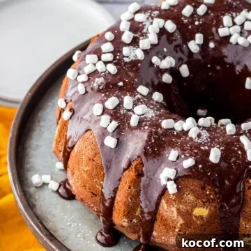 Finished Hot Chocolate Cake on metal cake stand with glaze and mini marshmallow bits.