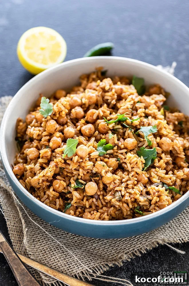 Instant Pot Brown Rice Chana Pulao Recipe 2 brown rice chana pulao served in a blue bowl, garnished with cilantro and a cut lemon and green chili in the background