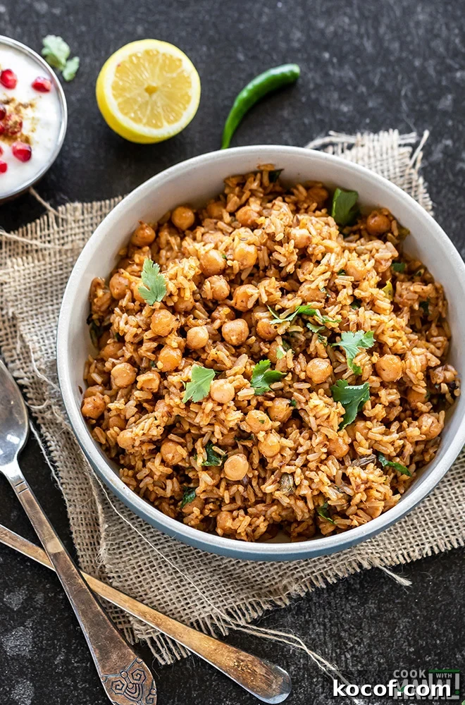 Instant Pot Brown Rice Chana Pulao Recipe 3 brown rice chana pulao in a bowl with 2 spoons on the side and a bowl of yogurt with pomegranate arils in the background