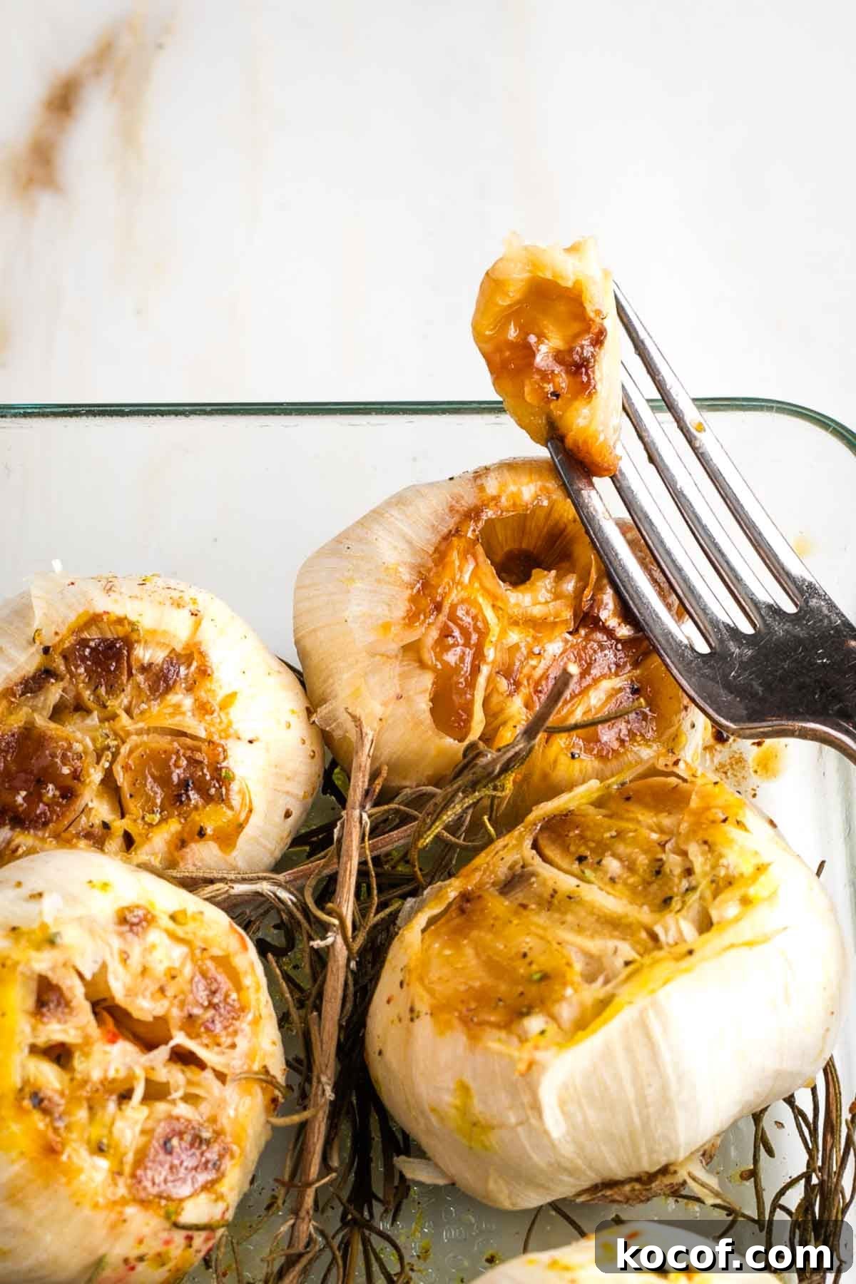 Oven-Roasted Garlic Bulbs: Crispy, Sweet Garlic Recipe 10 Pulling out one clove of roasted garlic from the entire bulb in a baking dish.