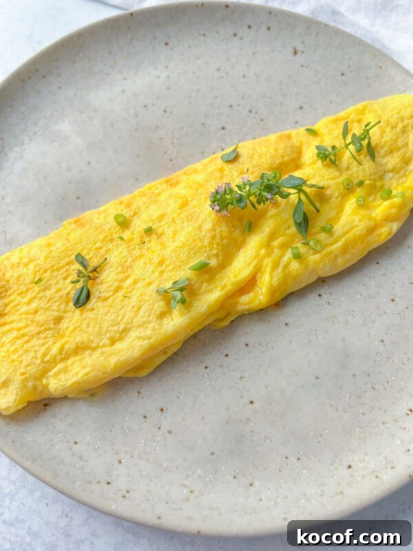 Perfect Hard-Boiled Eggs in the Air Fryer: Quick Guide 6 A neatly folded yellow omelet garnished with small green herbs sits on a speckled light gray ceramic plate.