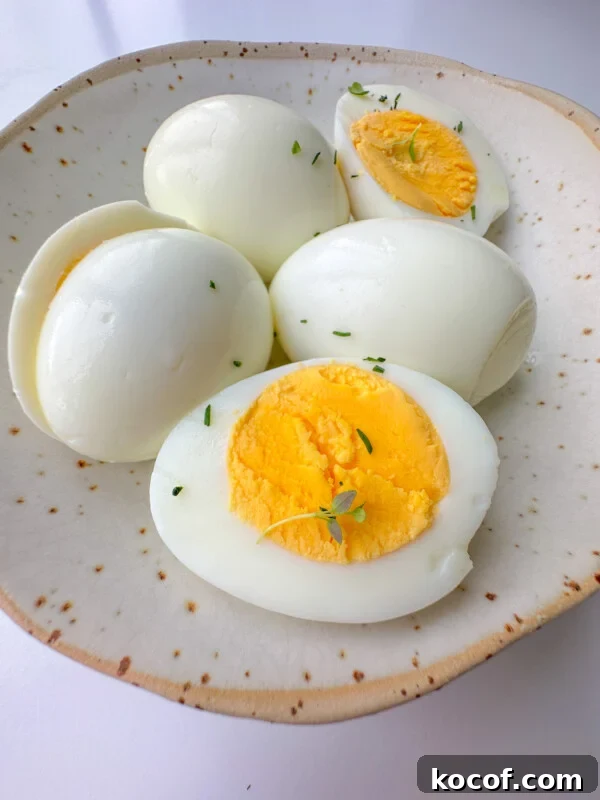 Perfect Hard-Boiled Eggs in the Air Fryer: Quick Guide 7 A ceramic plate holds four Easy Peel Hard Boiled Eggs, two sliced in half to reveal their bright yellow yolks.