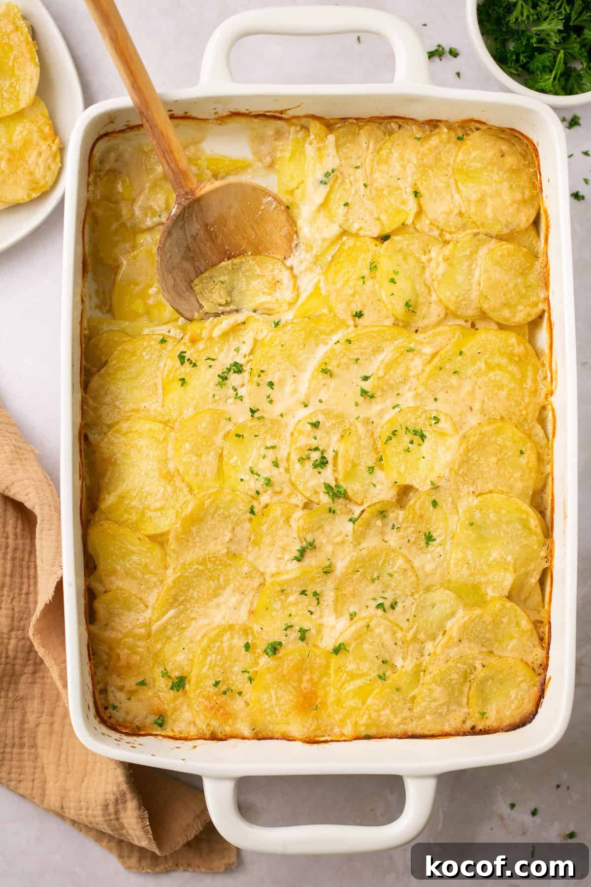 gluten free scalloped potatoes in a casserole dish with a wooden spoon taking a scoop out