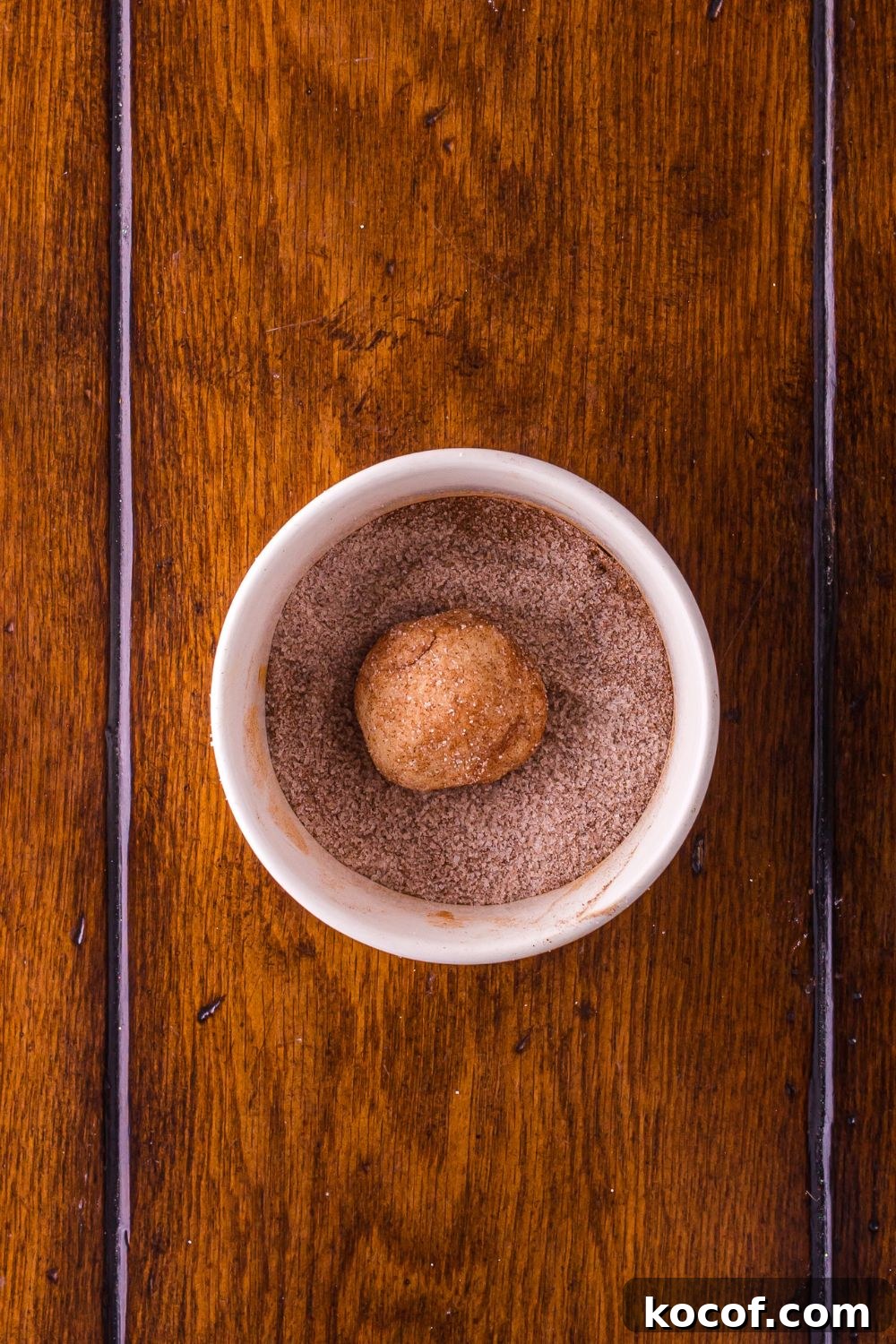 snickerdoodle cookie dough rolled in cinnamon sugar mixture in a white bowl on table 