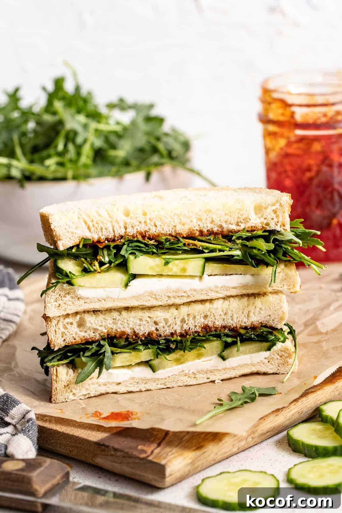 Stacked goat cheese and cucumber sandwiches next to a glass jar of sweet chili jam.