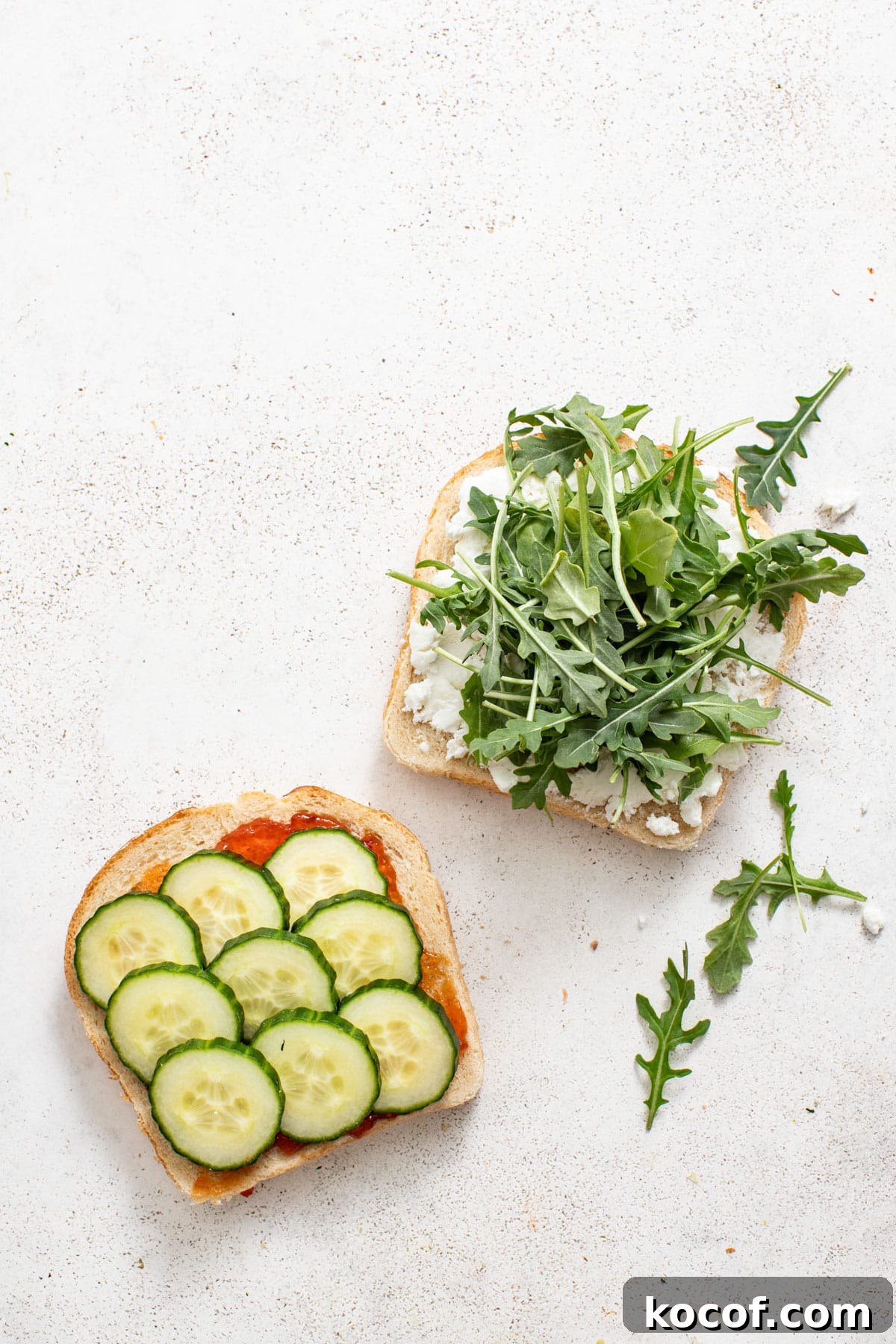 Layering cucumber and arugula on top of the cheese and bread.