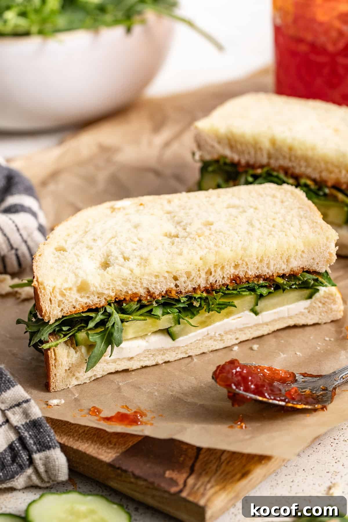 A goat cheese and arugula sandwich next to a spoon filled with pepper jelly.