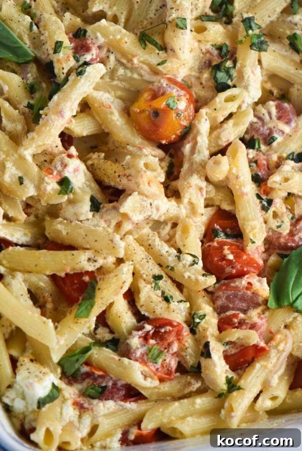 Baked goat cheese pasta in a white baking dish with tomatoes and basil.