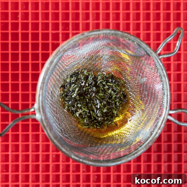 Rosemary-Infused Olive Oil: How to Make & Use It in Recipes 3 Straining rosemary leaves from the olive oil.