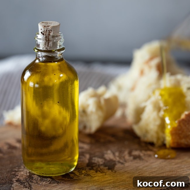 Rosemary-Infused Olive Oil: How to Make & Use It in Recipes 4 A small bottle of rosemary olive oil, with bread being drizzled with it in the background.