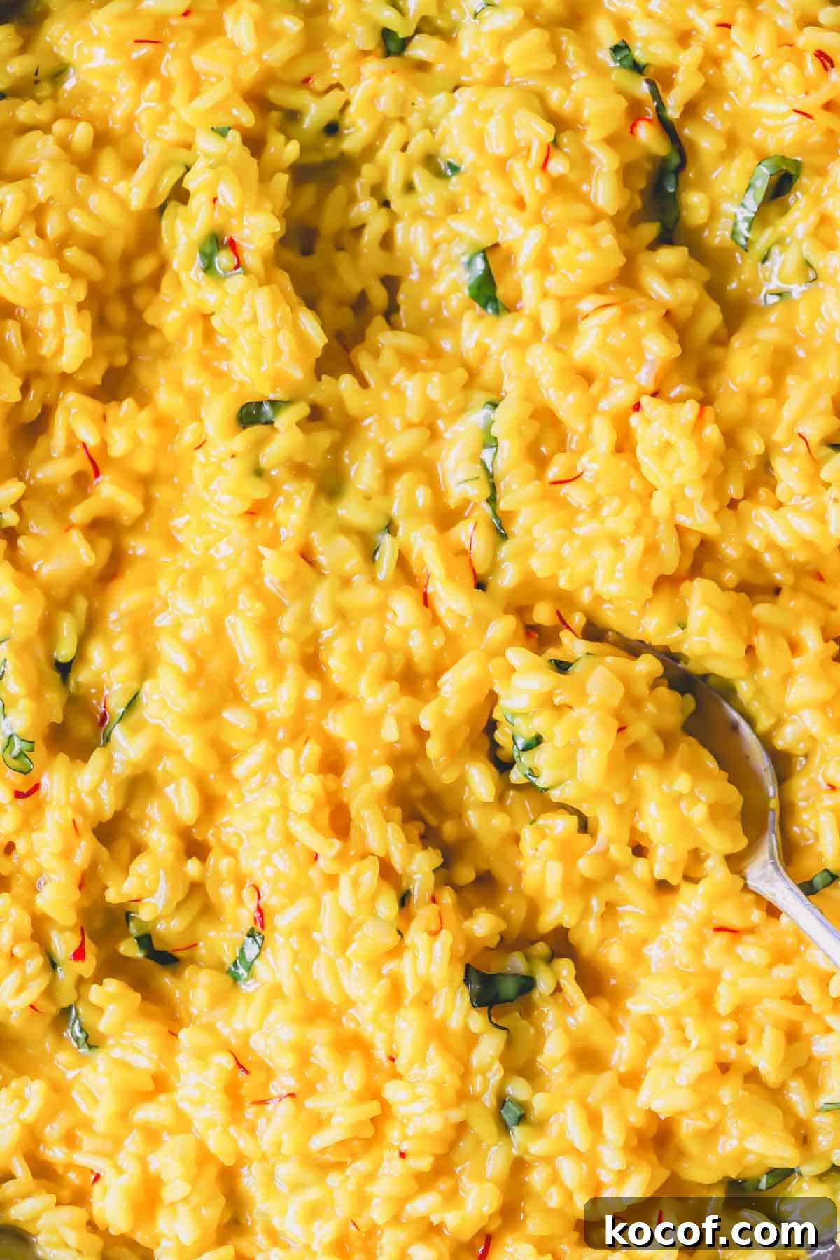 Close view of creamy saffron risotto with a spoon lifting a scoop.
