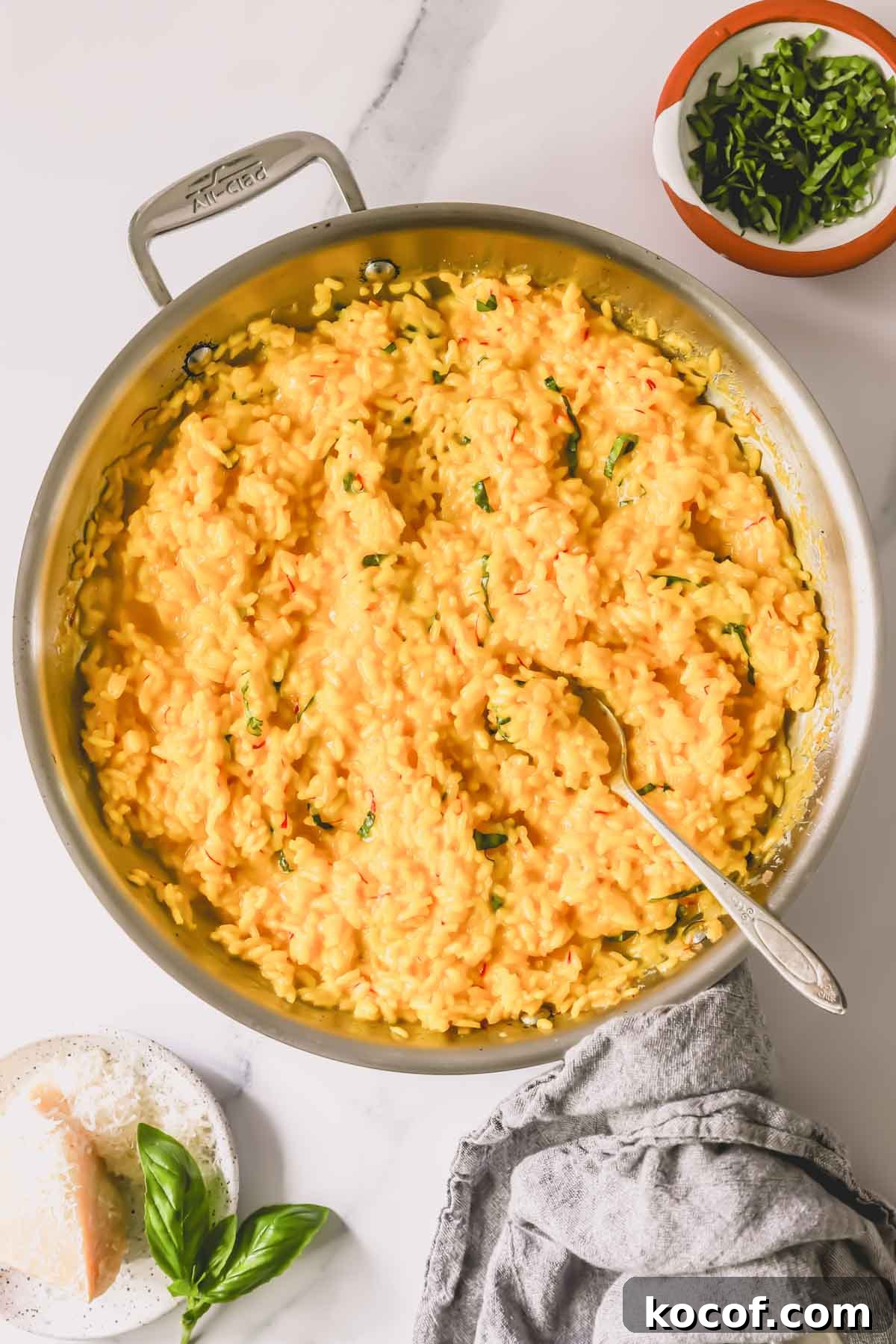 A pan of saffron risotto topped with fresh herbs with a spoon sticking out.