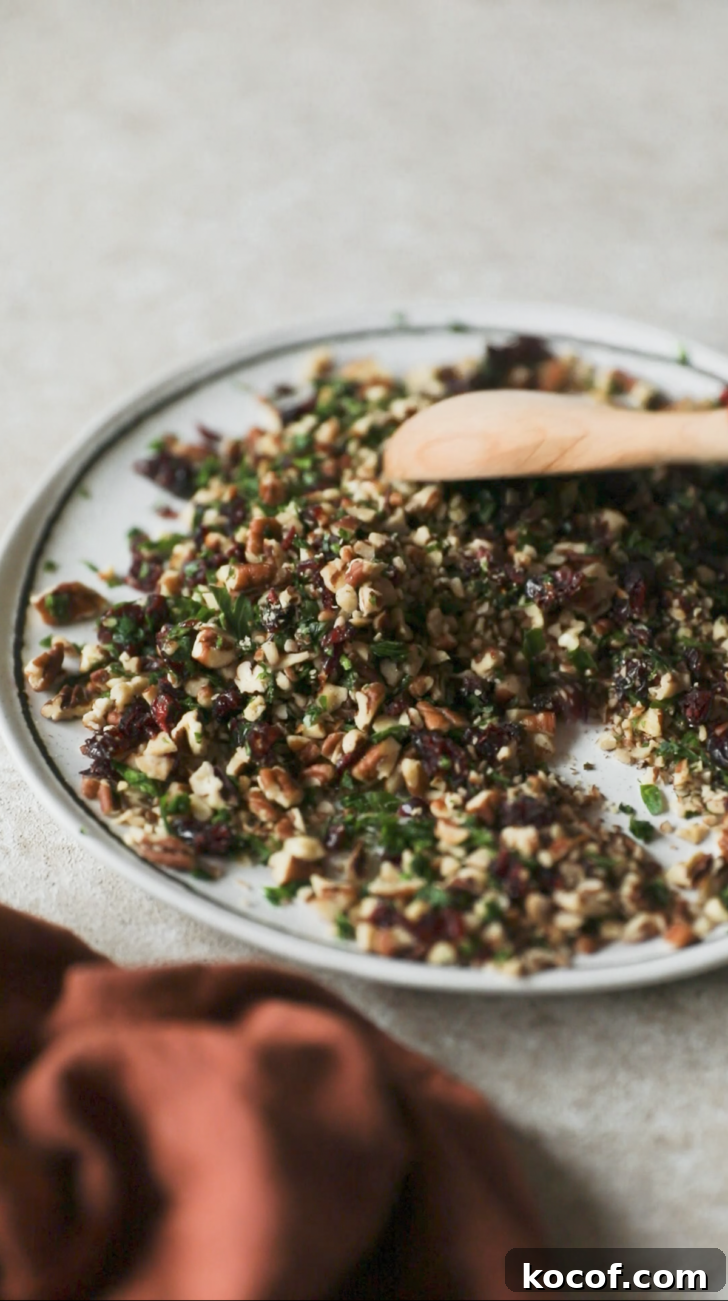 Cranberry Orange Cheesecake Bites: Festive Party Appetizer 8 A spoon mixing cranberries, pecans, and herbs on a white plate.