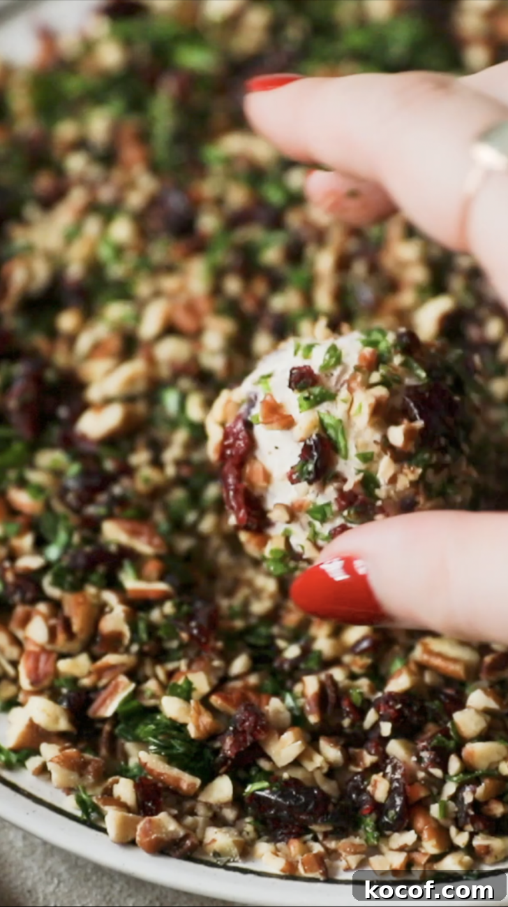 Cranberry Orange Cheesecake Bites: Festive Party Appetizer 9 A hand rolling cheese balls in herbs and nuts.