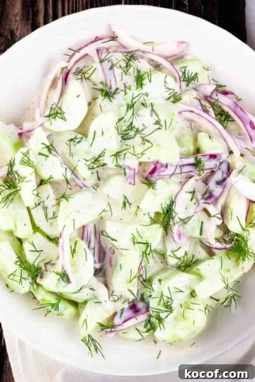 Creamy cucumber and onion salad in a white serving bowl.