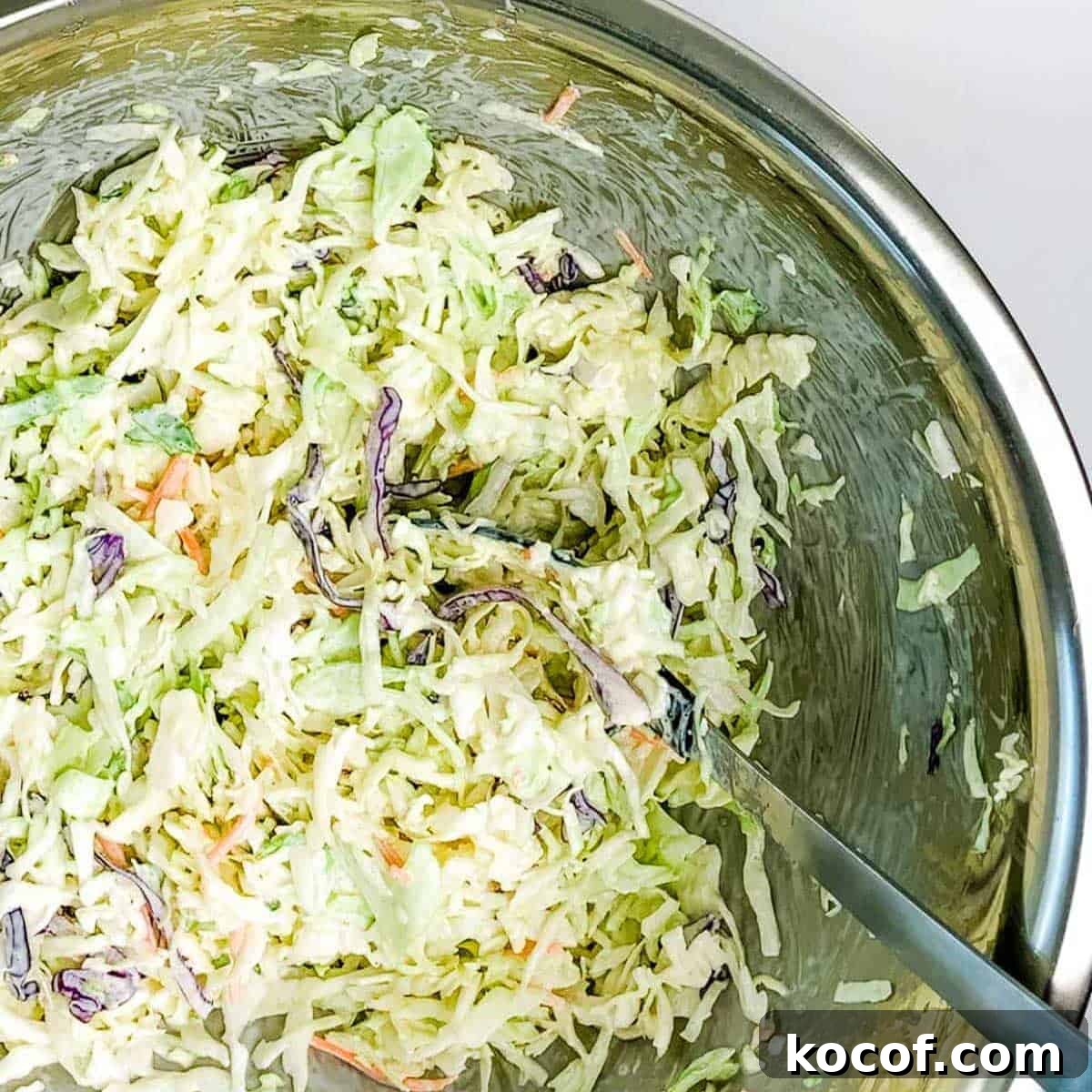 The ingredients for the slaw combined in a large bowl with a large spoon.