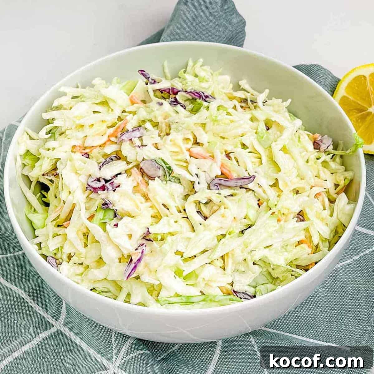 A white bowl filled with prepared Miracle Whip coleslaw with a lemon wedge in the background.