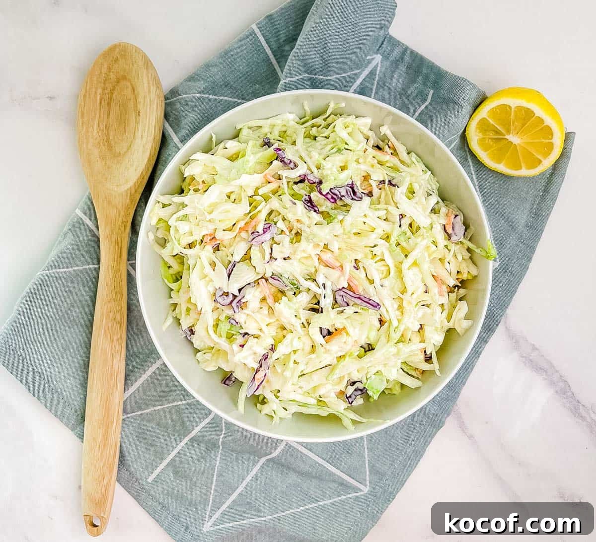 The creamy mayo coleslaw in a white bowl with a wooden spoon beside it.