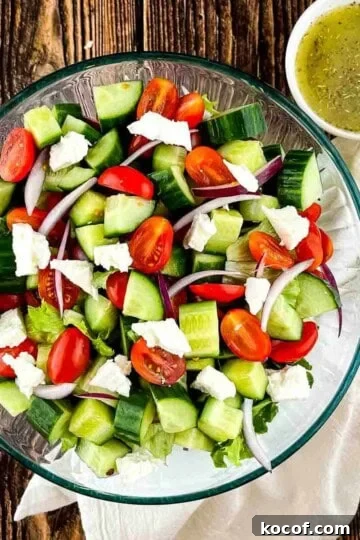A large glass bowl filled with Greek cucumber salad, with a small bowl of homemade dressing beside it.