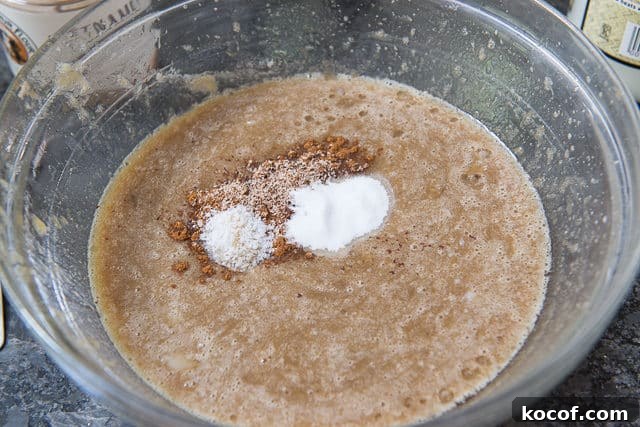 Pureed Banana Wet Ingredients in Glass Bowl with Cinnamon, Nutmeg, and Leavening On Top