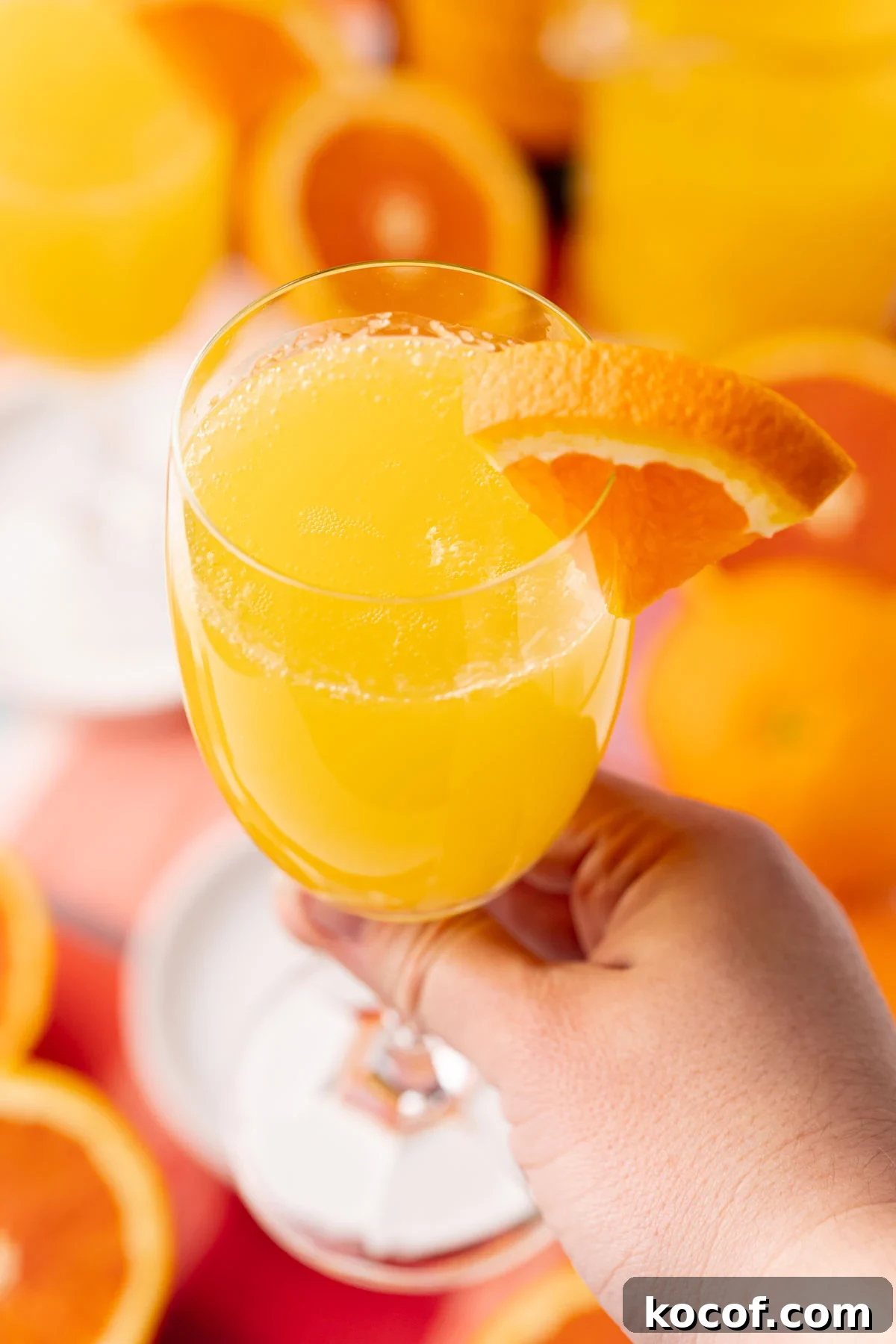 A woman's hand holding a mimosa to the camera.
